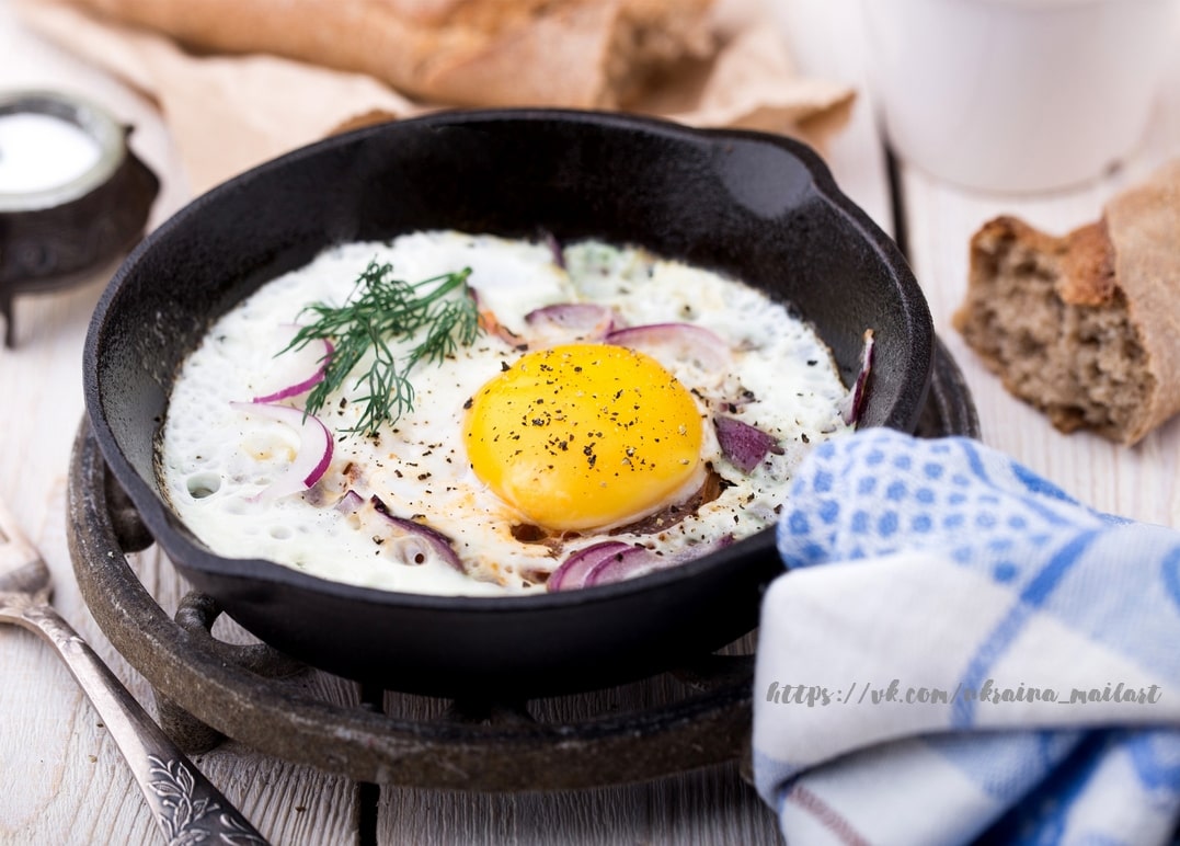 Fried egg in a cast-iron skillet with red onion rings and dill