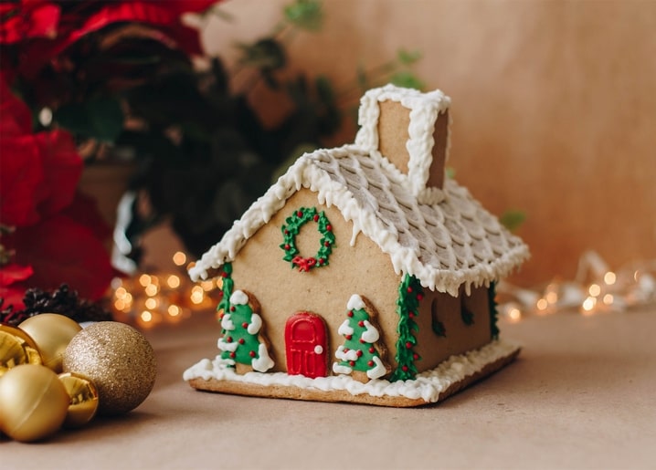 Lebkuchenhaus mit roter Tür und Kranz neben einem Weihnachtsstern und einer Lichterkette