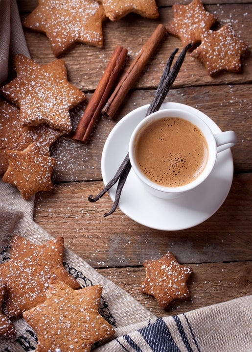 Sternförmige Lebkuchen mit Zimtstangen und Vanilleschoten neben einer Tasse Kaffee.