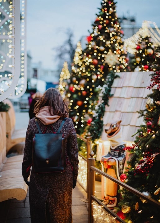 Mädchen mit Rucksack geht an beleuchteten Weihnachtsbäumen auf dem Markt vorbei