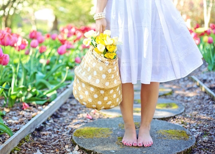 Frau im weißen Kleid mit Korb voller gelber Tulpen, barfuß im rosa Tulpengarten