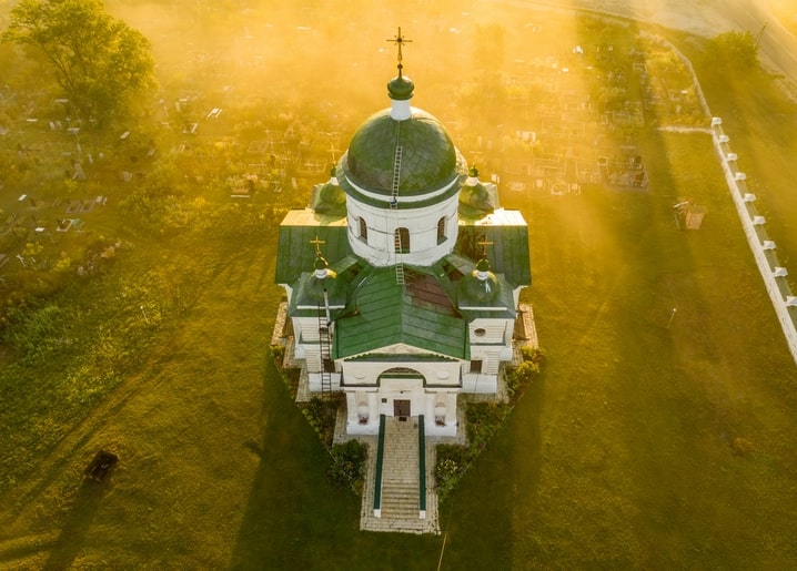 Вигляд з висоти на білу церкву з зеленими банями біля Мостища в золотому вечірньому світлі серед цвинтаря