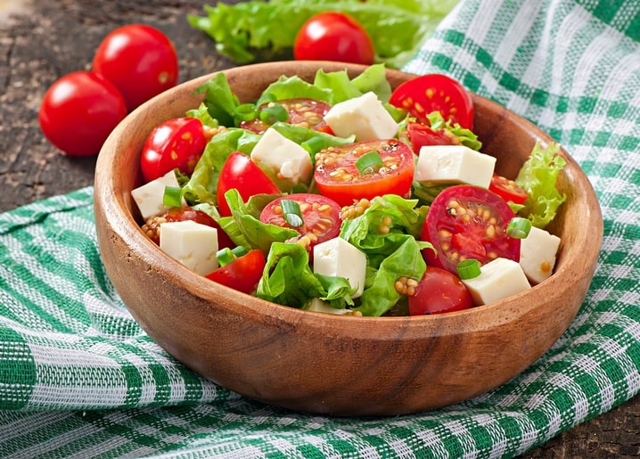 Greek salad with cherry tomatoes, feta cubes and lettuce in a wooden bowl on a checkered cloth