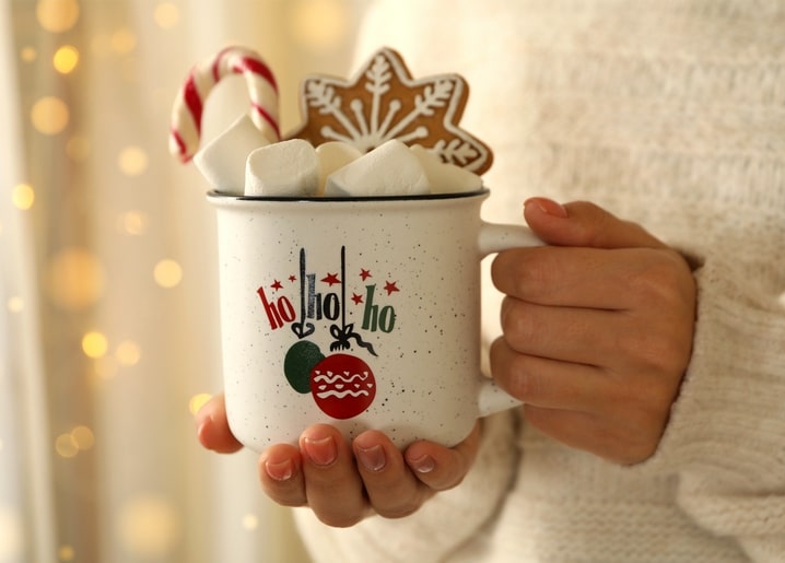 Hand hält weiße Tasse „Ho Ho Ho“ mit Zuckerstange und Lebkuchen-Schneeflocke