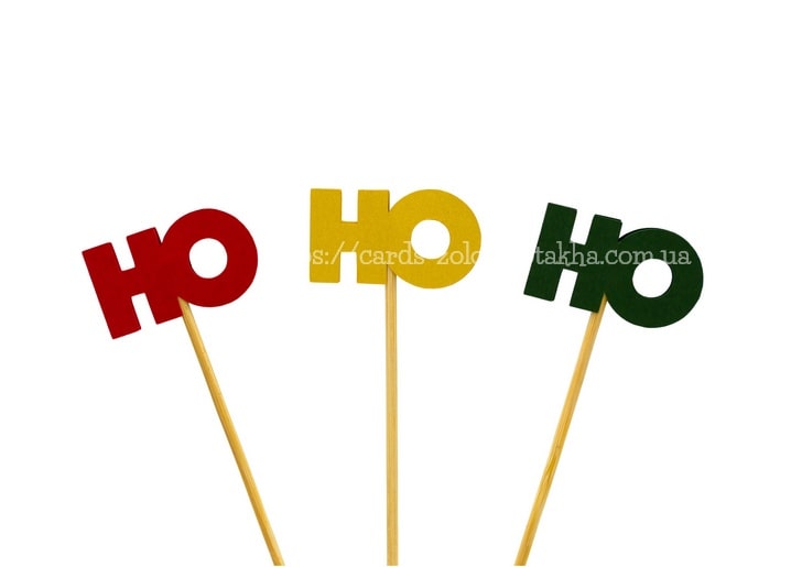 Rote, gelbe und grüne „Ho Ho Ho“-Cupcake-Topper auf Holzstäbchen vor weißem Hintergrund