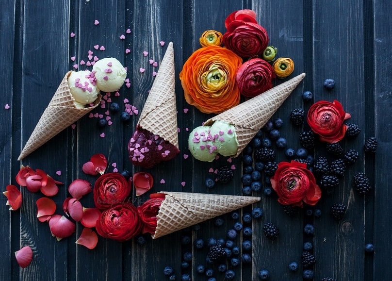 Eiswaffeln mit Eis zwischen Ranunkeln, Brombeeren und Blaubeeren auf dunklem Holz