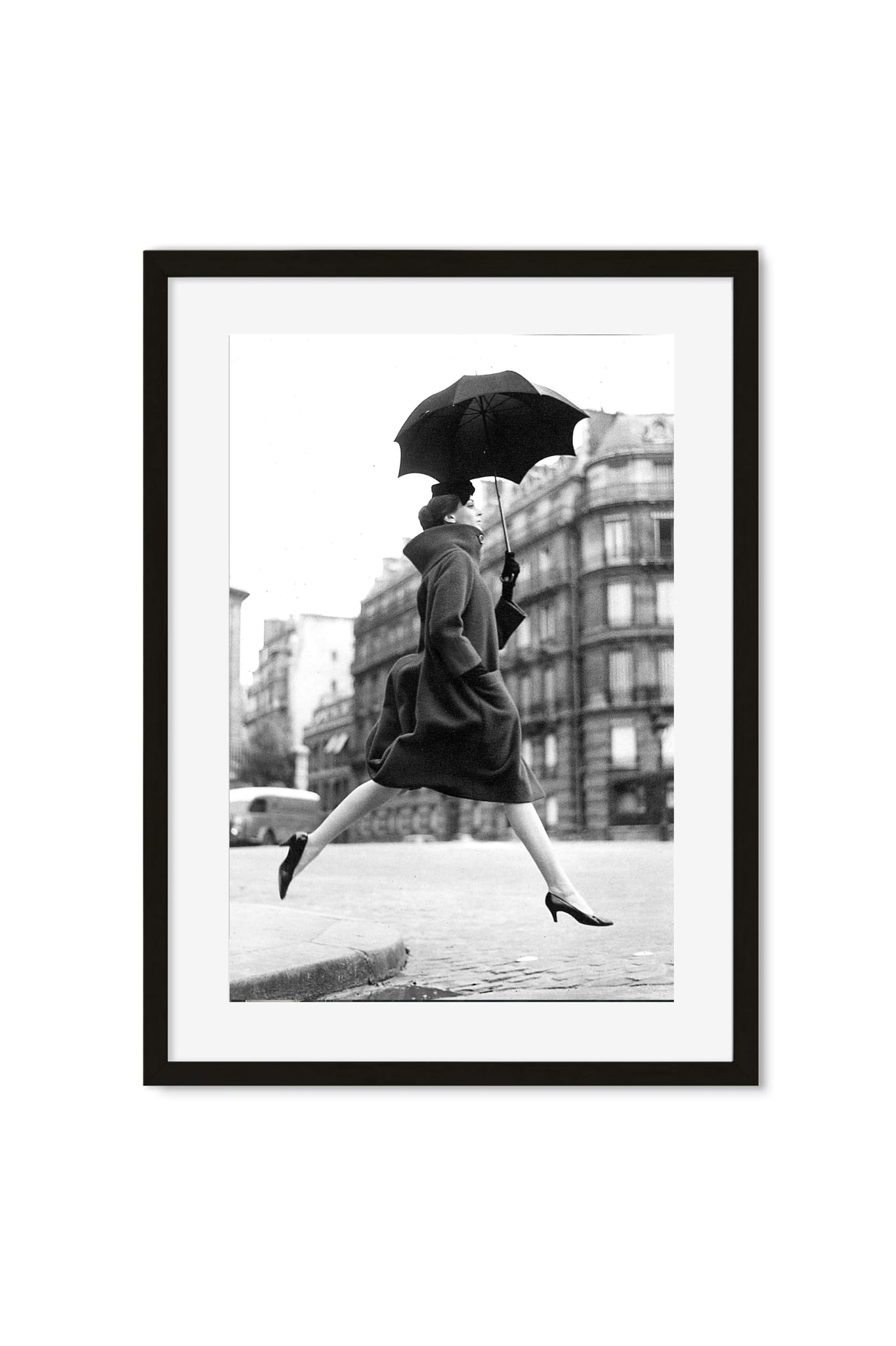 Black-and-white photo of a woman leaping with an open umbrella across a Paris street, framed poster