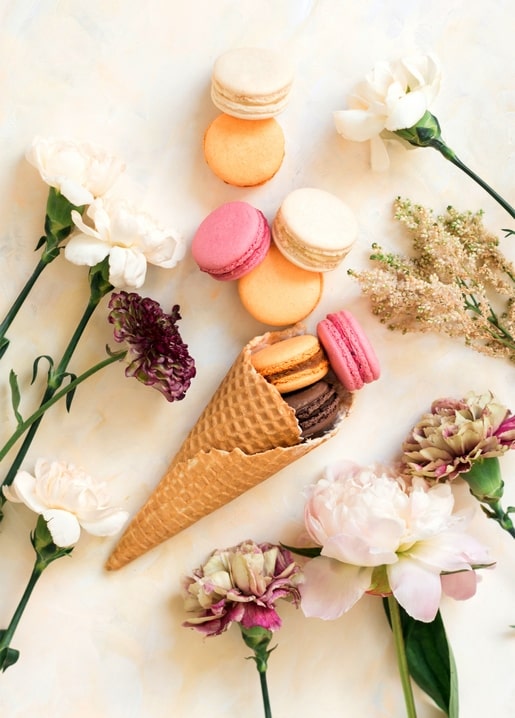 Waffeltüte mit bunten Macarons umgeben von Pfingstrosen und Nelken