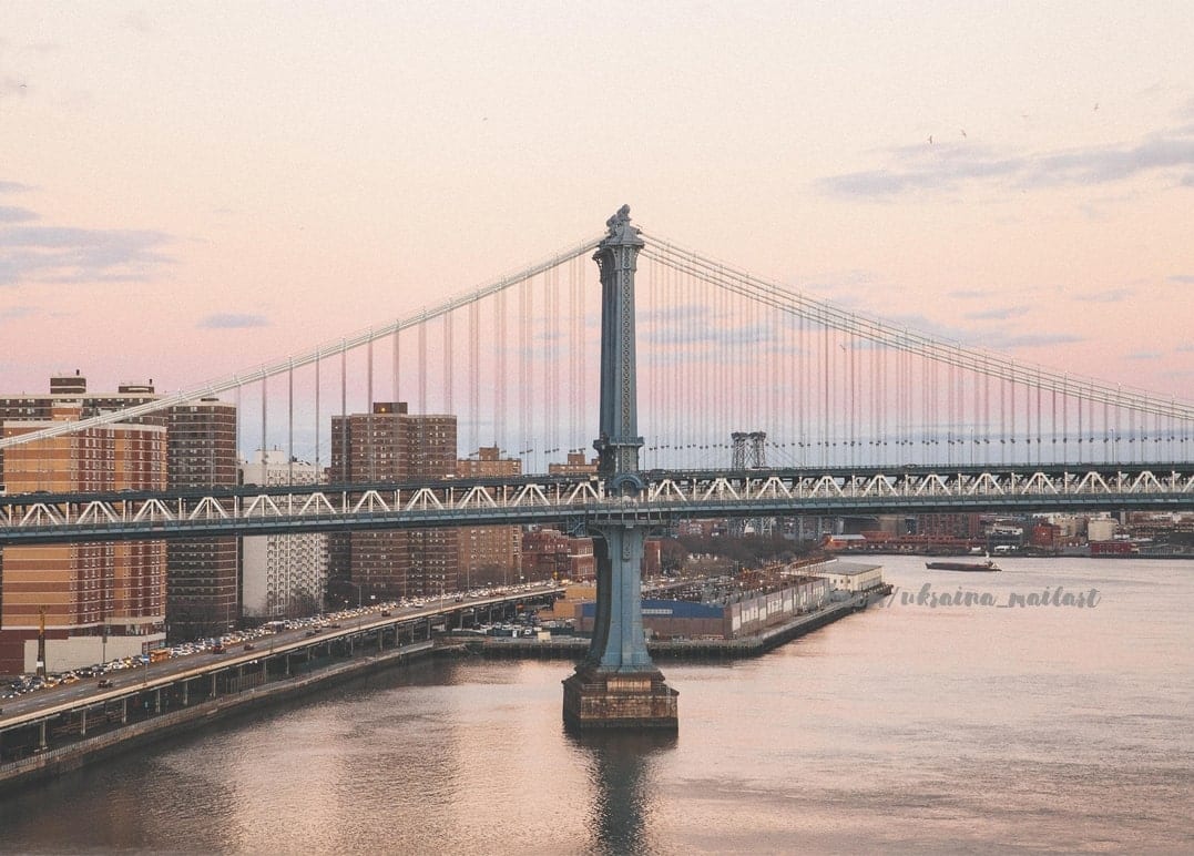 Die Manhattan Bridge vor rosafarbenem Abendhimmel über dem East River und der Skyline