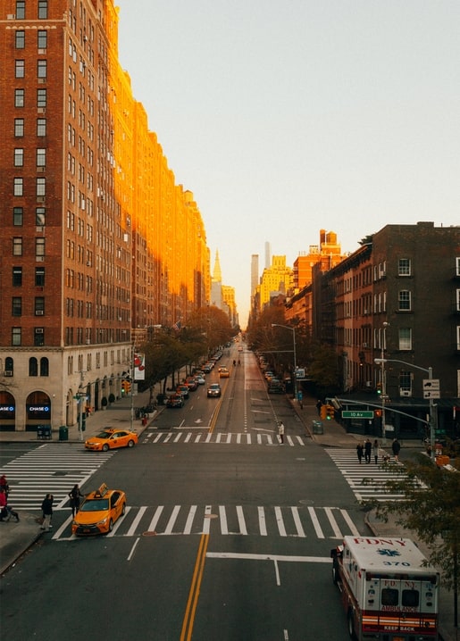 Sunset over a Manhattan street with brick buildings and yellow taxis at a crosswalk
