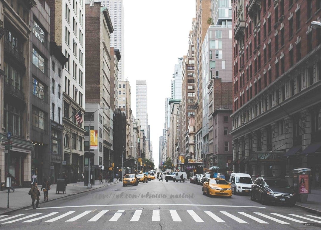Gelbe Taxis überqueren eine breite Straße in Manhattan zwischen Wolkenkratzern