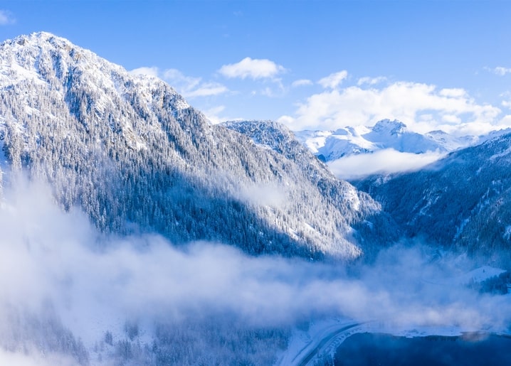 Schneebedeckte Berggipfel über einem nebelverhangenen Alpental