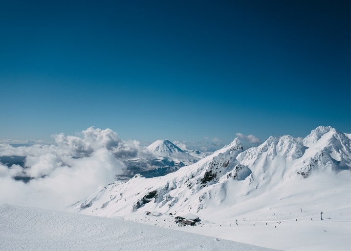 Schneebedeckte Berggipfel mit aufsteigenden Wolken und einer kleinen Skihütte