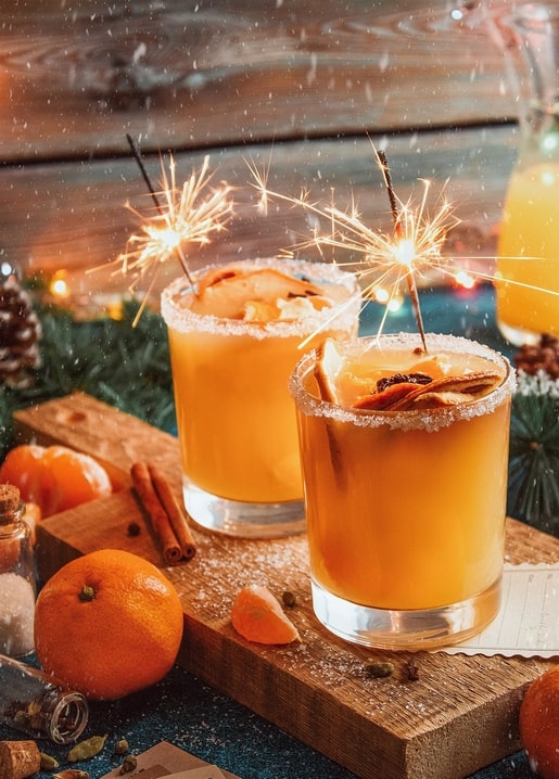 Zwei Gläser heißer Orangen-Cocktail mit Wunderkerzen, Zimtstangen und Orangenschale