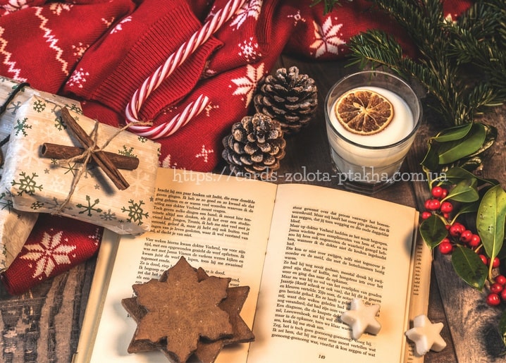 Aufgeschlagenes Buch auf rotem Schneeflocken-Strick mit Kerze und Tannenzapfen