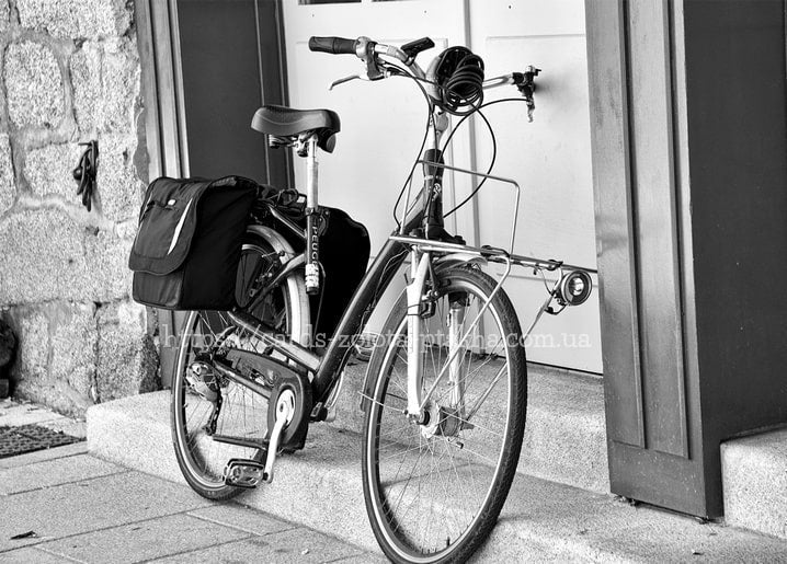 Schwarzweißfoto eines Peugeot-Fahrrads mit Gepäcktaschen vor einem Steinportal