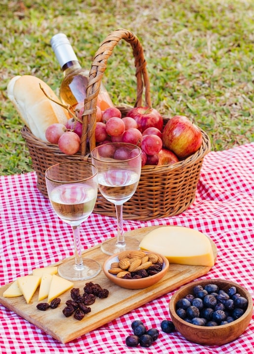 Wicker picnic basket with wine, baguette, grapes and apples on a checkered blanket