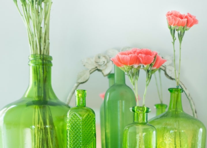 Rosa Nelken zwischen alten grünen Glasflaschen und Vasen