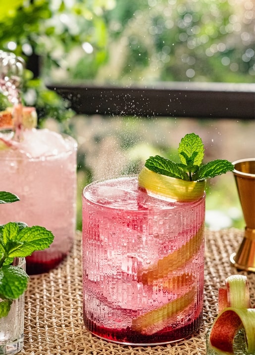 Prickelnder rosa Cocktail mit Minze und Rhabarber auf einem Gartentisch
