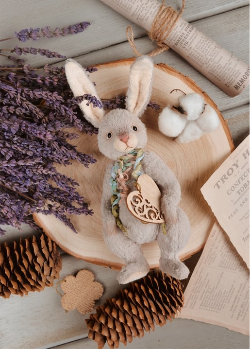 A plush bunny with a wooden heart charm sitting among lavender and pinecones