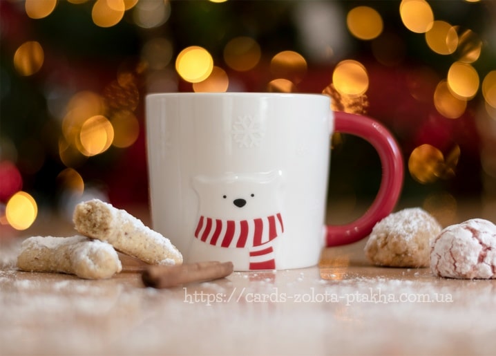 Weiße Eisbär-Tasse mit rotem Schal neben Puderzucker-Plätzchen und einem Zimtstab