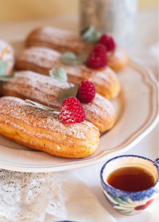 Teller mit Himbeer-Eclairs neben einer Tasse Tee