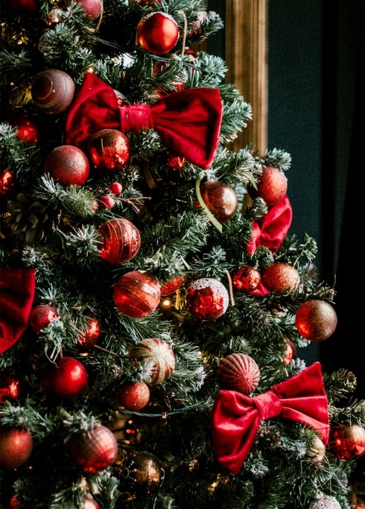 Nahaufnahme eines Weihnachtsbaums mit roten und goldenen Christbaumkugeln und roten Samtschleifen