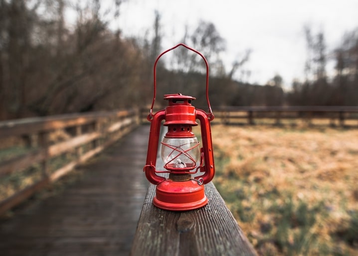 Red vintage lantern hanging on a wooden fence rail over a misty autumn field