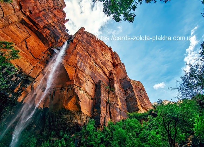 Wasserfall an einer roten Sandsteinwand im Canyon vor blauem Himmel