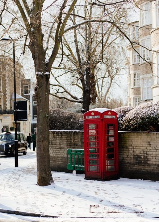 Rote Telefonzelle auf einer verschneiten Londoner Straße zwischen kahlen Bäumen.