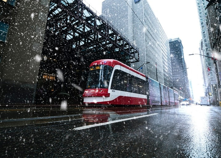 Rot-weiße Straßenbahn fährt durch Schneetreiben auf einer Stadtstraße
