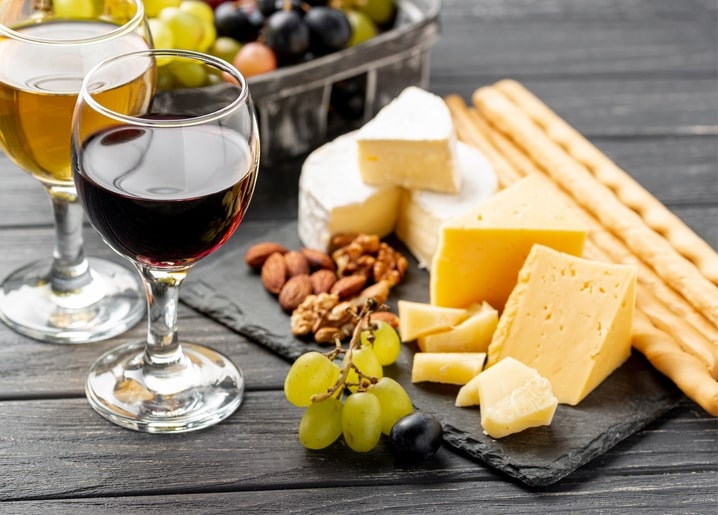 Two wine glasses with cheese cubes, grapes, walnuts, almonds and breadsticks