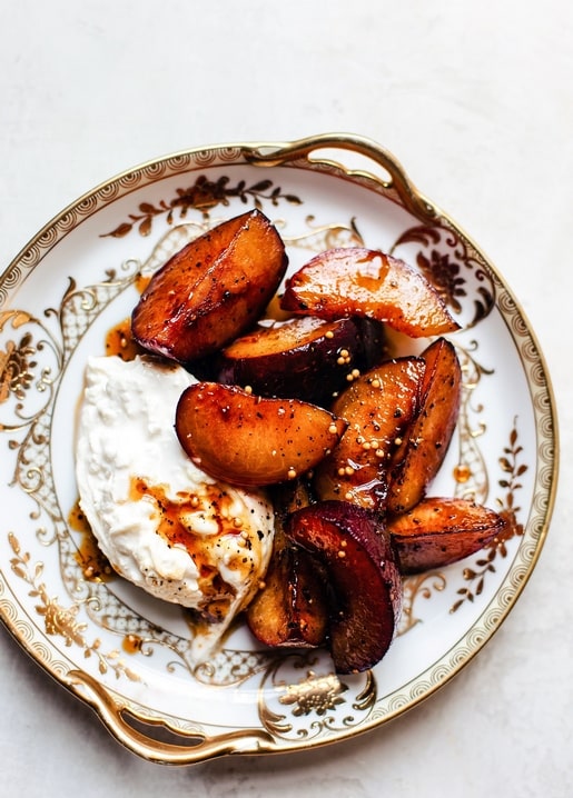 Caramelized roasted plum wedges served over creamy burrata on a gold-rimmed vintage plate.
