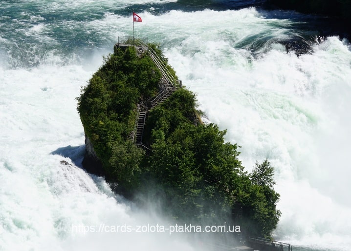 Tree-covered rock island with a staircase and flag amid raging waterfall rapids