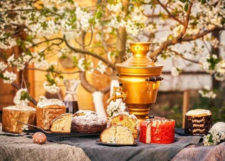 Goldener Samowar und aufgeschnittenes Osterbrot auf einem Tisch unter blühenden Zweigen