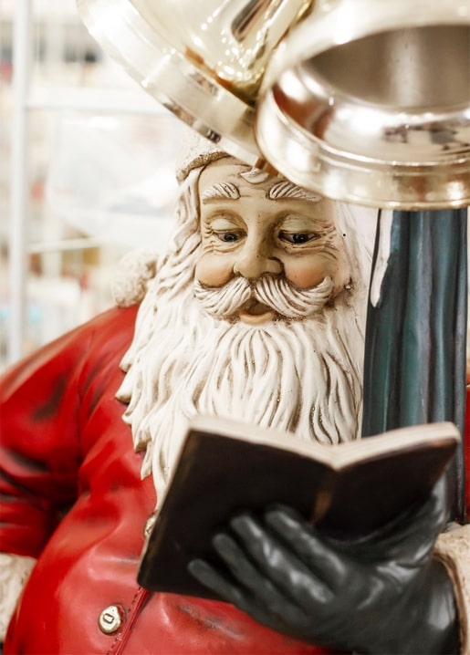 Nahaufnahme einer Weihnachtsmann-Figur, die mit behandschuhter Hand ein Buch aufschlägt.