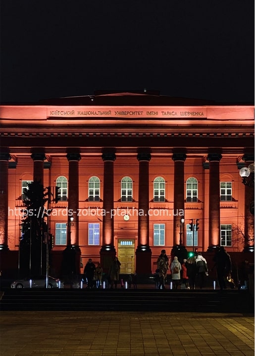 Red-lit columned facade of Taras Shevchenko University in Kyiv at night with holiday lights