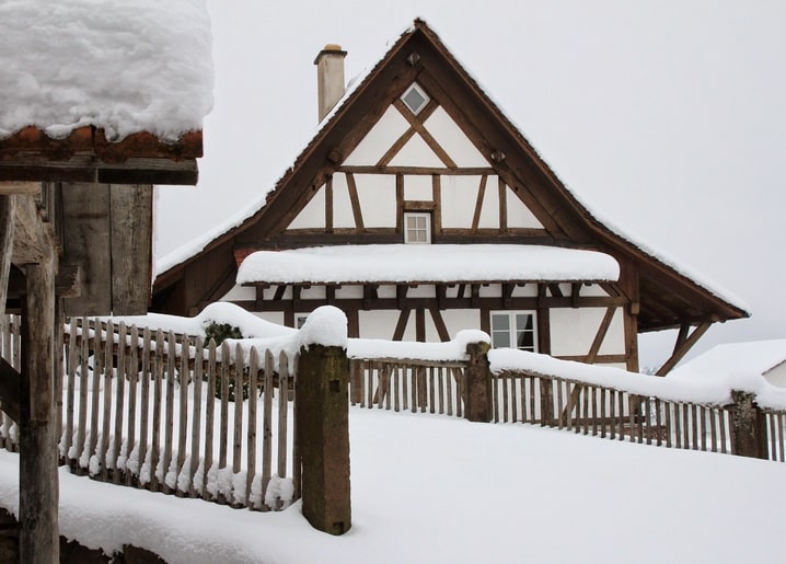 Snow-covered half-timbered house behind a frosted wooden picket fence