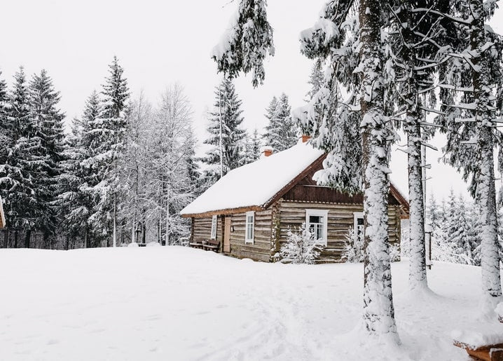 Snow-covered wooden log cabin surrounded by frosted pine trees in a winter forest