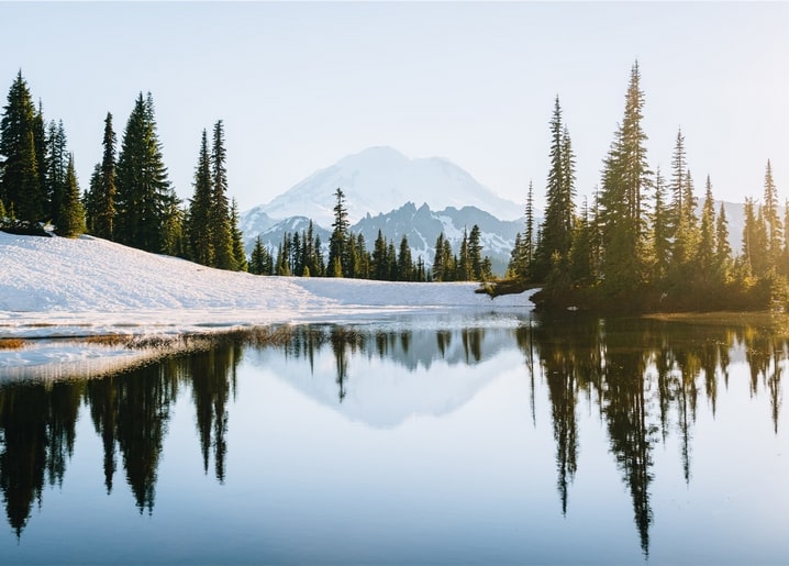 Schneebedeckte Kiefern und Berggipfel spiegeln sich in ruhigem See