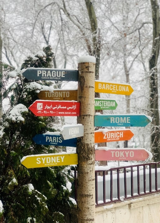 Schneebedeckter Wegweiser mit Pfeilen nach Prag, Paris, Tokio und weiteren Städten