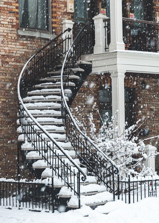 Schneebedeckte schmiedeeiserne Wendeltreppe an einem Backsteinhaus im Schneefall