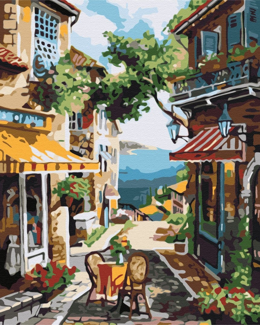 Sunlit street in a southern Mediterranean town with café awning, iron balcony and hillside view