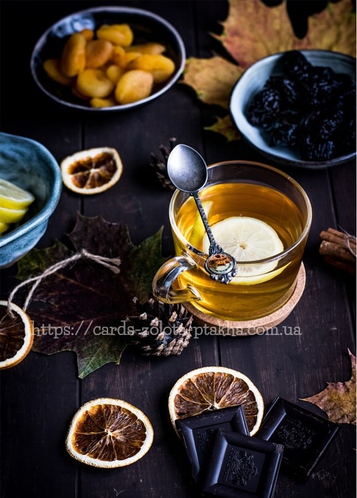 Teetasse mit Zitrone zwischen getrockneter Orange, Zimt, dunkler Schokolade und Herbstlaub