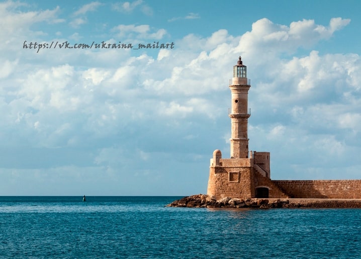 Steinerner Leuchtturm am Rand einer türkisfarbenen Bucht unter teils bewölktem Himmel