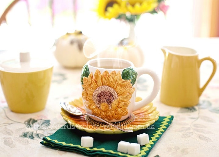 Sunflower-patterned mug of steaming tea beside sugar cubes and a cream jug