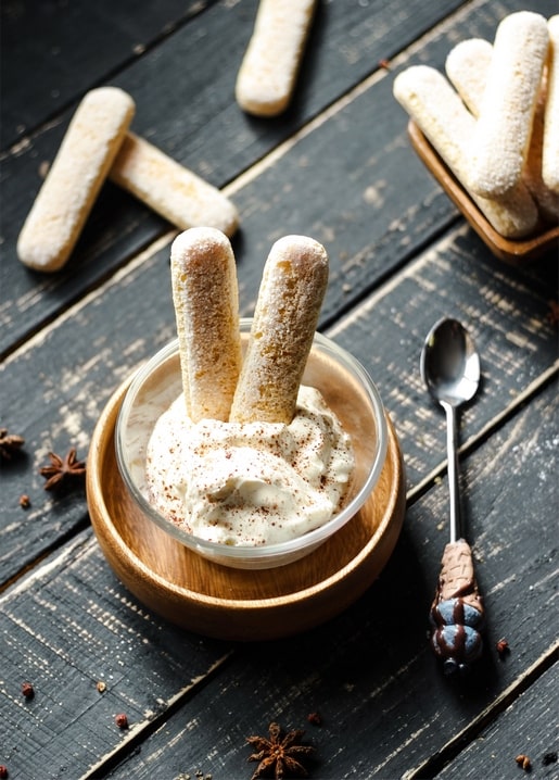 Schale Tiramisu mit Kakao neben Löffelbiskuits und einem Löffel