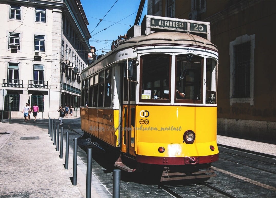 Gelbe Tram Nummer 25 fährt eine sonnige Straße in Lissabon entlang