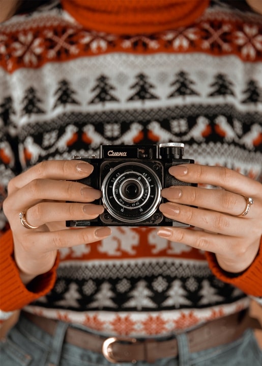 Hands in a red Fair Isle Christmas sweater holding a vintage folding camera