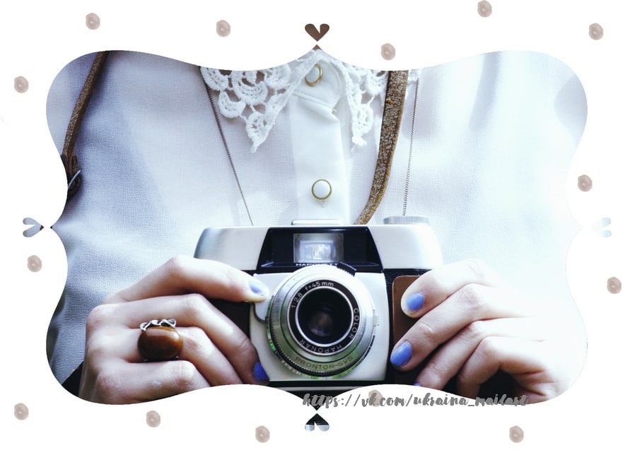 Hands with blue nail polish holding a vintage film camera against a lace-collared blouse